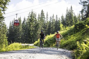Zwei Mountainbiker auf Schotterweg unter roter Gondelbahn am Fulseck in grüner Berglandschaft | © SalzburgerLand, Heiko Mandl