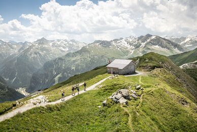 Wandergruppe auf Bergpfad bei Holzhütte mit Ausblick auf schneebedeckte Gipfel in Gastein | © Gasteinertal Tourismus GmbH