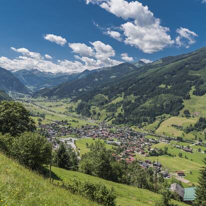 Weitblick auf Dorfgastein mit grünen Wiesen, bewaldeten Bergen und Gasteinertal unter blauem Himmel | © Gasteinertal Tourismus GmbH