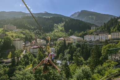 Frau schwebt an der Flying Waters Zipline über die Dächer von Bad Gastein mit Blick auf Wälder und Berge | © Max Steinbauer Photography