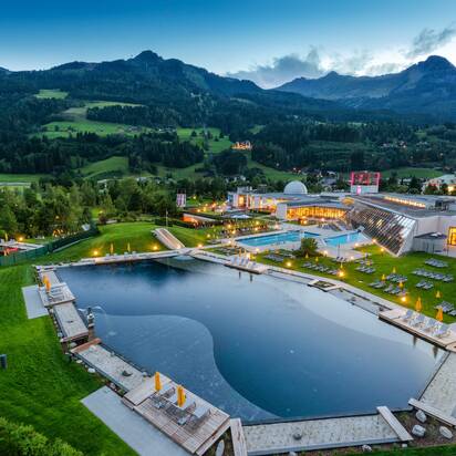 Abendaufnahme der Alpentherme Gastein mit beleuchtetem Badesee und grüner Berglandschaft im Hintergrund