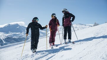 Three people in ski gear are standing on a slope talking with smiles | © Gasteinertal Tourismus GmbH, Christoph Oberschneider