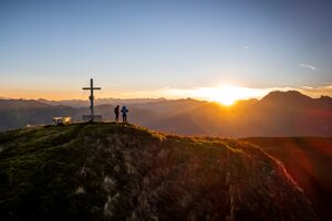 Zwei Wanderer am Gipfelkreuz im Großarltal bei Sonnenaufgang mit weitem Blick auf Berggipfel und goldenem Morgenlicht. | © Tourismusverband Großarltal 