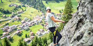 Frau am Klettersteig oberhalb von Großarl mit Blick auf Dorf, Wiesen und bewaldete Berge im Tal | © Gipfelfieber