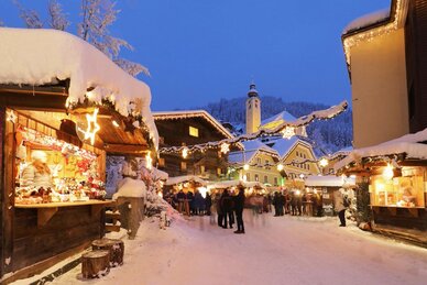Lit advent stalls at Salzburg Mountain Advent in Grossarl with visitors, church and snow covered houses | © Tourismusverband Großarltal