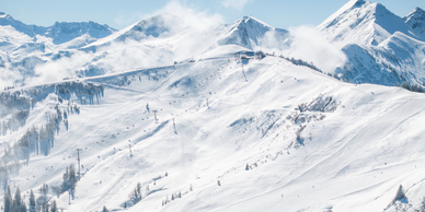 Wide view of the Grossarltal ski area with groomed slopes, lifts, snowy peaks and drifting mountain clouds | © Lorenz Masser