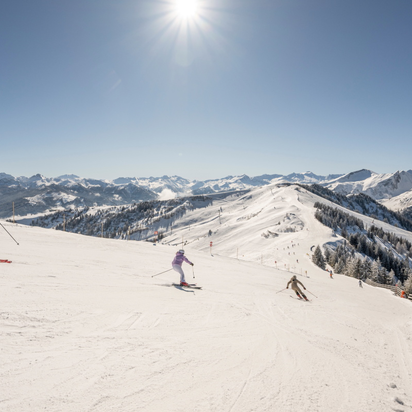 Three skiers descend a wide groomed slope in Grossarltal ski area with snowy mountains under bright sun | © Lorenz Masser
