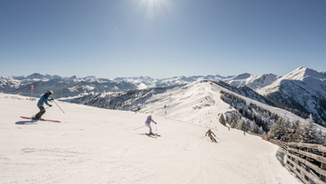 Three skiers descend a wide groomed slope in Grossarltal ski area with snowy mountains under bright sun | © Lorenz Masser
