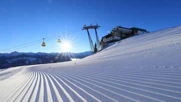 The rising sun illuminates the freshly prepared piste and the cable car passes over it | © Tourismusverband Großarltal