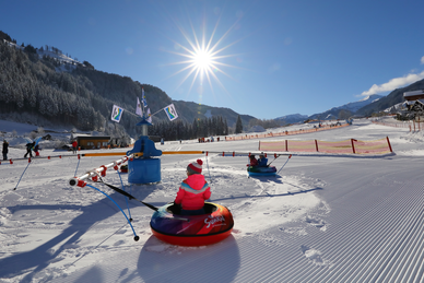 Kids ride tubing carousel on the snowy adventure meadow in Grossarltal under bright sunshine