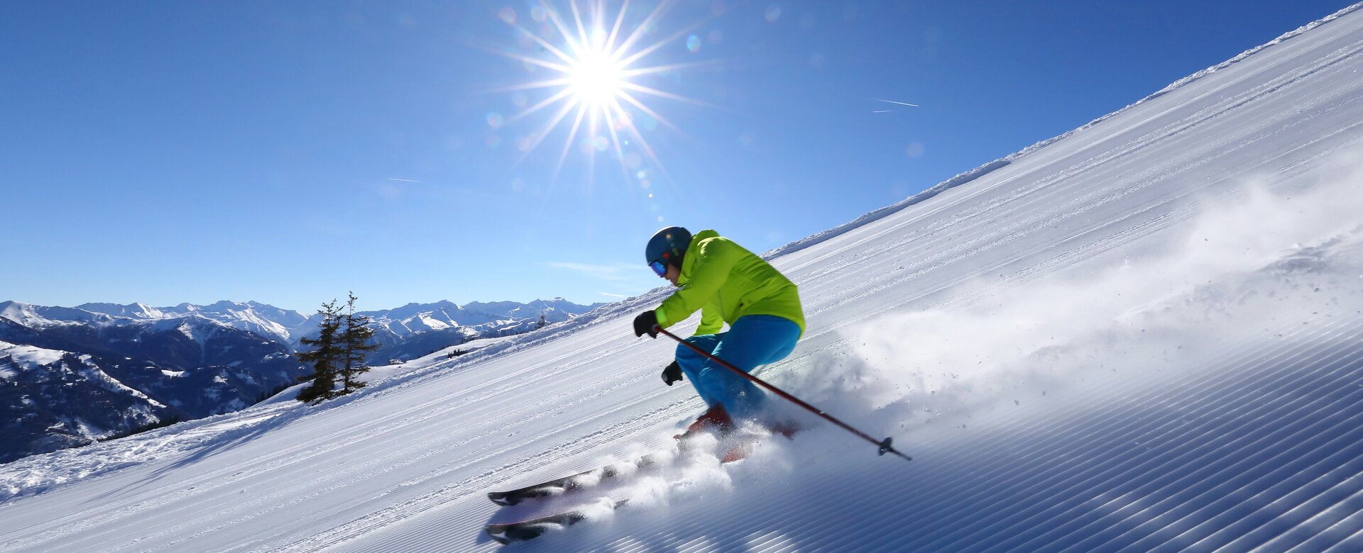 Skifahrer fährt über eine frisch präparierte Piste und wirbelt hinter sich Schneestaub auf und im Hintergrund ist ein schneebedecktes Bergpanorama | © Tourismusverband Großarltal
