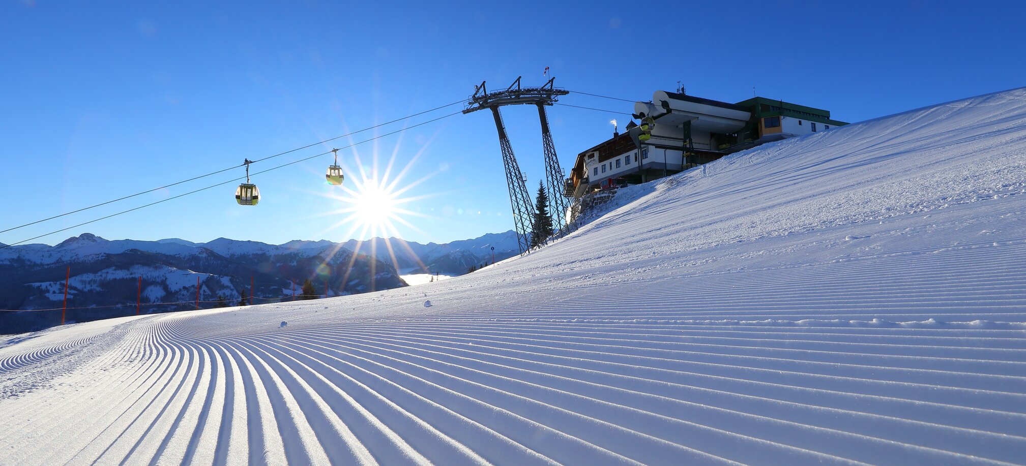 The rising sun illuminates the freshly prepared piste and the cable car passes over it | © Tourismusverband Großarltal