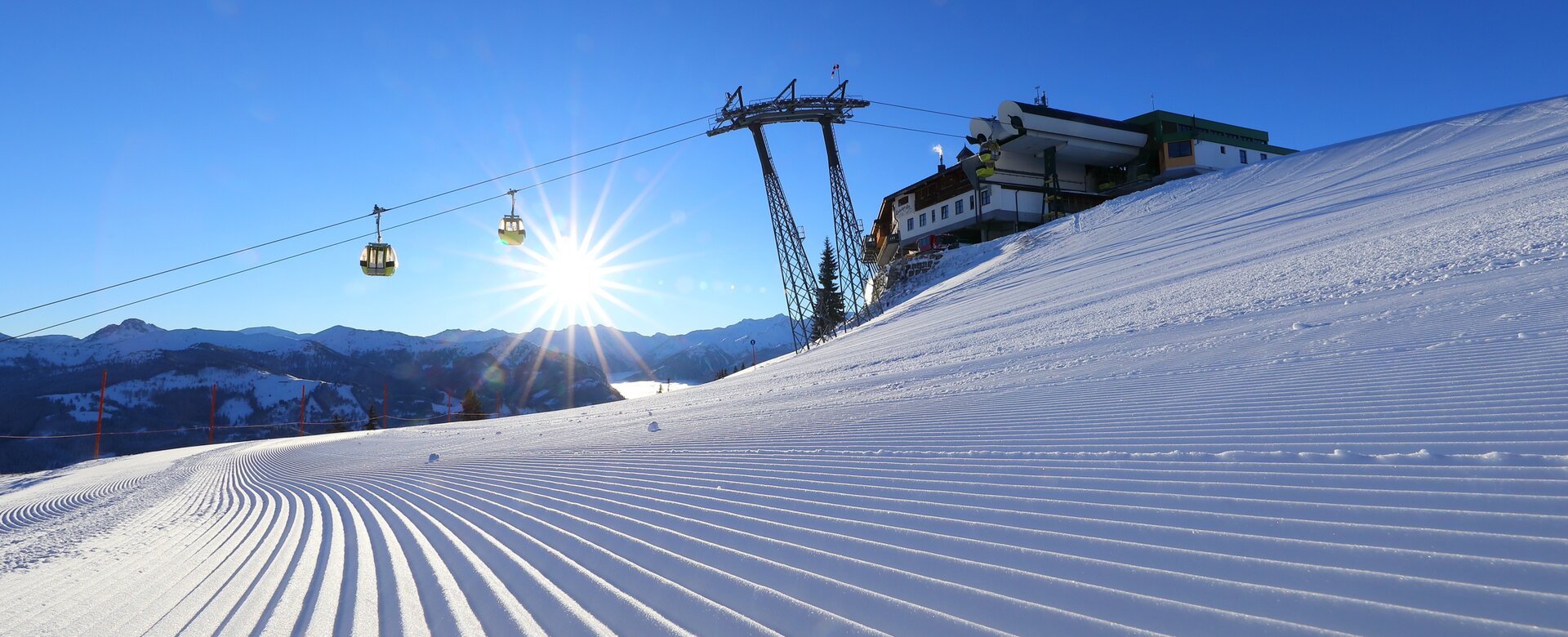 The rising sun illuminates the freshly prepared piste and the cable car passes over it | © Tourismusverband Großarltal