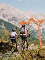 Zwei Mountainbiker fahren auf einem Schotterweg auf einen Torbogen zu, vor hohen Felsbergen in der Region Hochkönig. | © Hochkönig Tourismus GmbH
