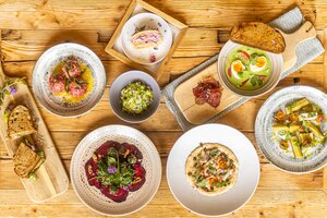 Several plated dishes with bread, soup, salad and dessert are arranged on a rustic wooden table. | © Hochkönig Tourismus GmbH