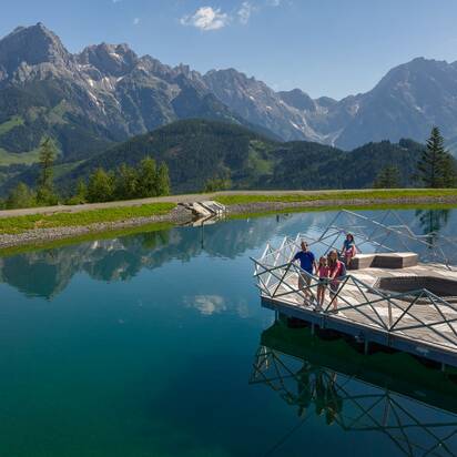 Family on wooden platform at Prinzensee in Maria Alm, clear lake water and Hochkönig mountains in background | © Roland Haschka