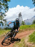 Ein Mountainbiker fährt durch eine Kurve auf einem Dirttrail zwischen Bäumen vor Bergen in der Region Hochkönig. | © Hochkönig Tourismus GmbH