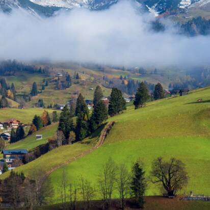 Weiße Kirche bei Dienten auf grünem Hügel, im Hintergrund der verschneite Hochkönig über nebelverhüllten Tälern