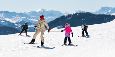 Adult skiing with three kids on wide sunny slope in the Alps | © Hochkönig Tourismus GmbH