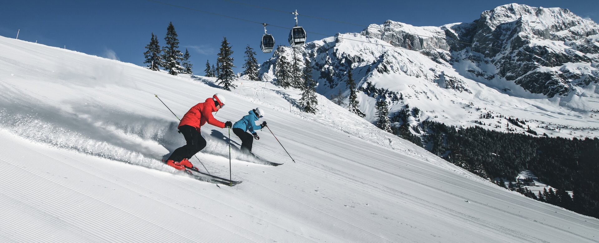 Zwei Skifahrer auf der Piste mit Gondel im Hintergrund | © Hochkönig Tourismus GmbH