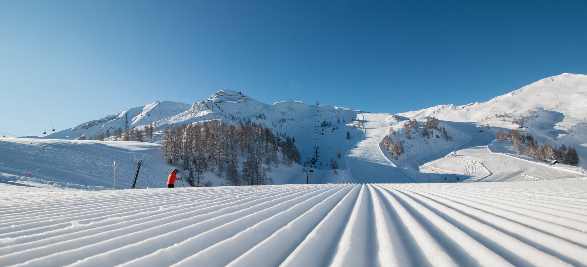 Freshly groomed piste with a view of the higher-lying piste landscape and the snow-covered surroundings