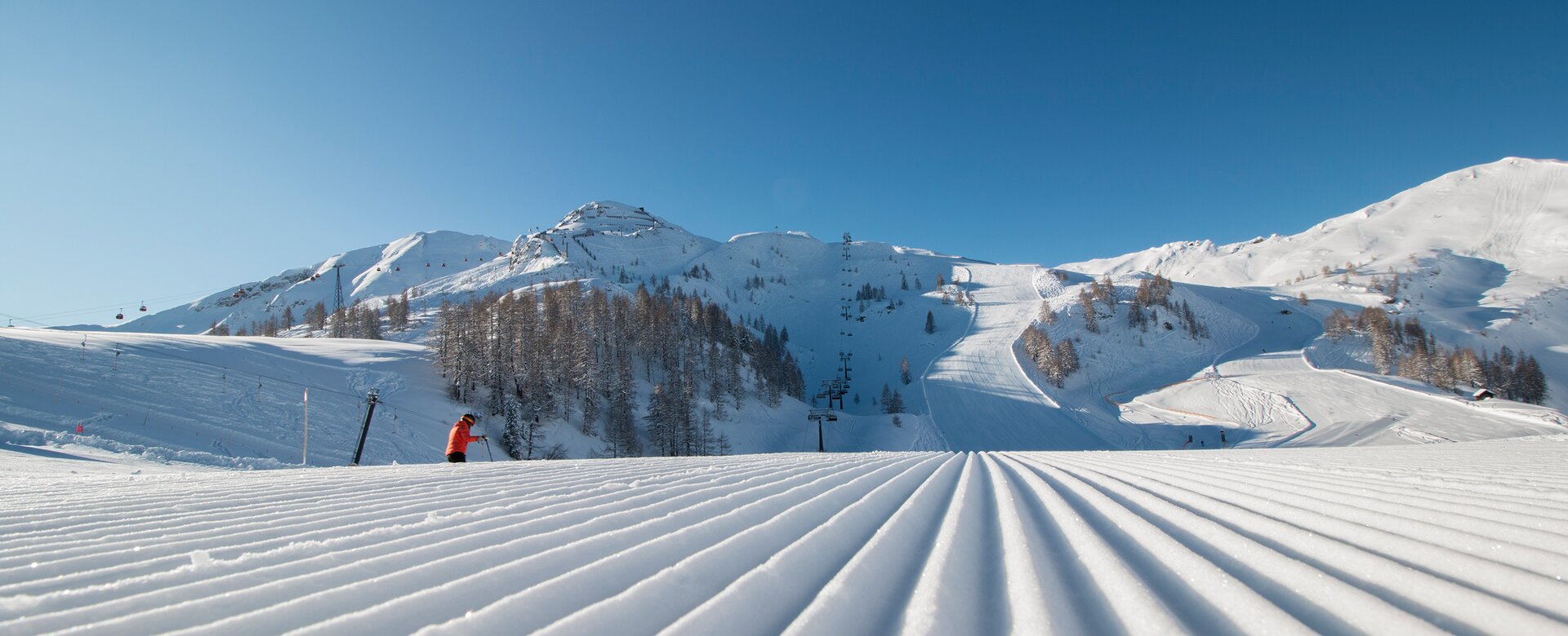 Freshly groomed piste with a view of the higher-lying piste landscape and the snow-covered surroundings