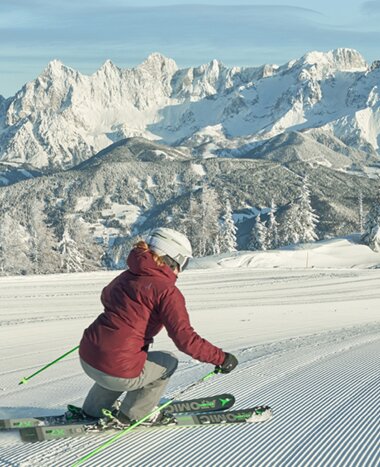 A skier descends the freshly prepared piste and the snow-covered Dachstein massif can be clearly seen in the distance. | © Schladming-Dachstein Peter Burgstaller