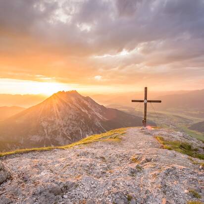 Summit cross at sunrise overlooking Gröbming area, mountain scenery bathed in golden morning light | © Christoph Huber