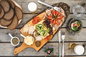 Herzhafte Brettljause mit Käse, Speck, Gemüse, Butter, Brot und Bier auf Holzbrett serviert, dazu Salat im Einmachglas | © Mathäus Gartner