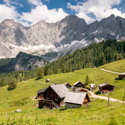 Traditional alpine huts of Neustattalmen on green meadows with the striking Dachstein massif towering in the background | © Schladming-Dachstein