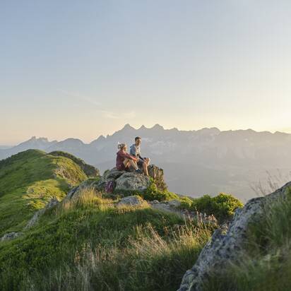 Zwei Wanderer sitzen auf einem Felsen und blicken beim Sonnenaufgang über die Berge der Reiteralm | © Peter Burgstaller