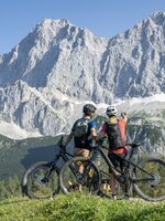 Zwei Mountainbiker mit Helmen und Rucksäcken stehen vor den Neustattalmen und blicken auf das Dachsteinmassiv | © Lorenz Masser