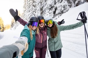 Three female skiers smiling for a selfie on a snow-covered slope in the mountains | © Mirja Geh