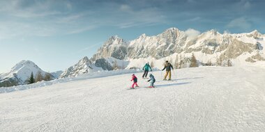Two adults and two kids skiing in front of snowy Dachstein massif in the Austrian Alps | © Peter Burgstaller