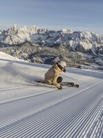 Skier carving deep turn on freshly groomed slope with panoramic mountain backdrop | © Mirja Geh
