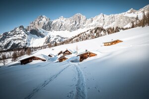 Footprints lead to snow-covered alpine huts below Dachstein mountains in wintry alpine landscape | © Mathäus Gartner
