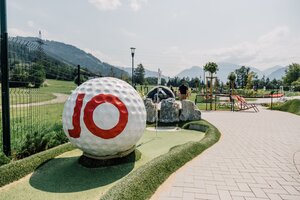 Minigolfbahn mit grossem Golfball, Flagge, Felsen und Wegen vor Wiesen, Bergen und blauem Himmel. | © JOSalzburg
