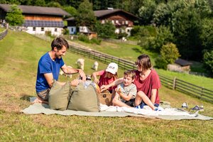 Familie beim sommerlichen Picknick auf grüner Wiese mit Bauernhäusern und Weide im Hintergrund | © TVB Eben