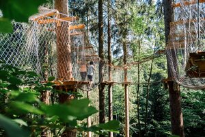 Two people walk through a high ropes course with hanging bridges and platforms among tall trees. | © JOSalzburg