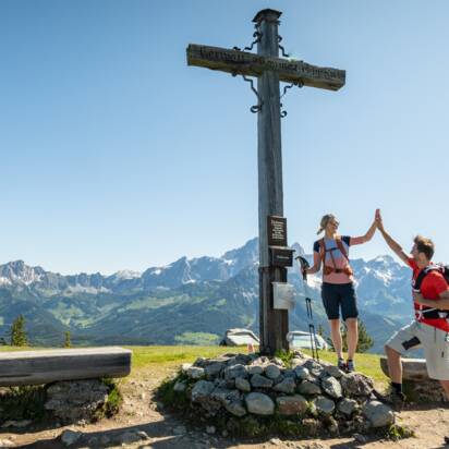 Zwei Personen stehen auf einem Plateau bei einem Gipfelkreuz und geben sich ein High Five | © Tourismusverband Radstadt/Lorenz Masser