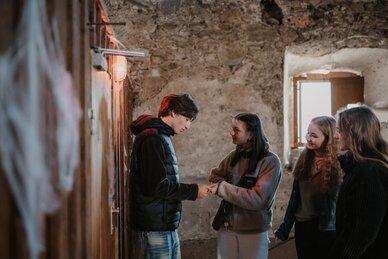 Four teenagers stand in an old stone room in Radstadt, looking together at an object held in their hands | © Tourismusverband Radstadt/Nadia Jabli
