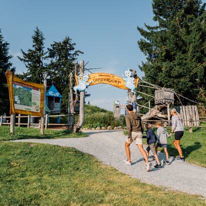 Familie mit zwei Kindern betritt bei Sonnenschein den fantasievollen Eingang zum Geisterberg mit Holzschild und Geisterfiguren