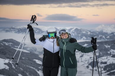 Zwei Skifahrerinnen posieren mit Skistöcken vor winterlicher Bergkulisse bei Sonnenuntergang | © Salzburger Sportwelt/Lorenz Masser