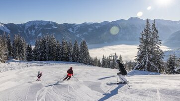 A family is skiing down the piste and the valley is covered in fog, while a bright blue sky can be seen above | © Michael Grössinger