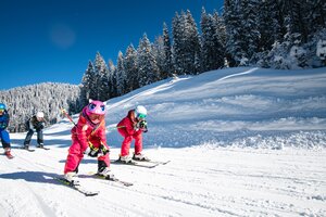 Zwei Kinder fahren in der Hocke mit den Skiern einen Ziehweg entlang und die Elter folgen direkt dahinter | © Salzburger Sportwelt, Christian Schartner