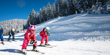 Two children crouch down on their skis and ski along a tow path with their parents following right behind them | © Salzburger Sportwelt, Christian Schartner