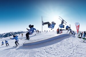 A freeskier does a frontflip over a rail at Cash4Tricks during RIDE Ski amadé, captured as a multiple-frame sequence.