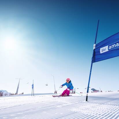 Skifahrerin fährt Slalom durch blaue Tore auf frisch präparierter Piste bei Sonnenschein in Ski amadé