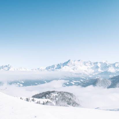 A skier looks out over snowy mountains and a vast sea of clouds in bright winter sun