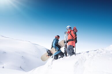 Two winter sports enthusiasts stand with skis and snowboard on a snowy mountain peak